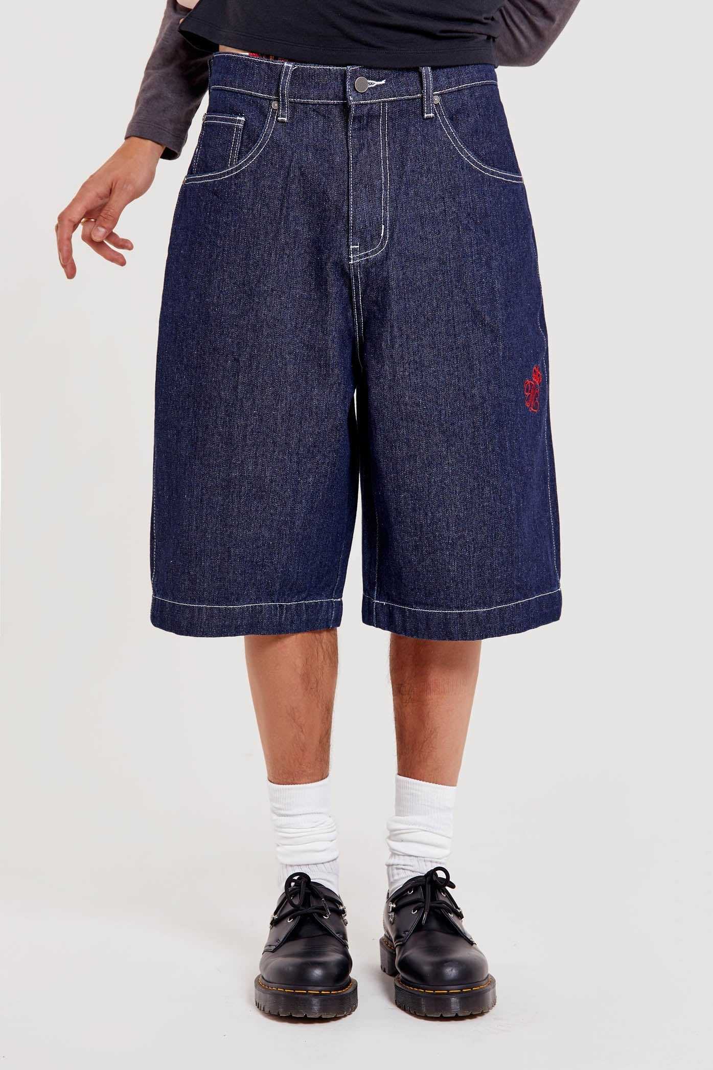 Male wearing indigo blue denim jorts in a jumbo fit with JL embroidered logo and Union Jack start branding on back pocket. 