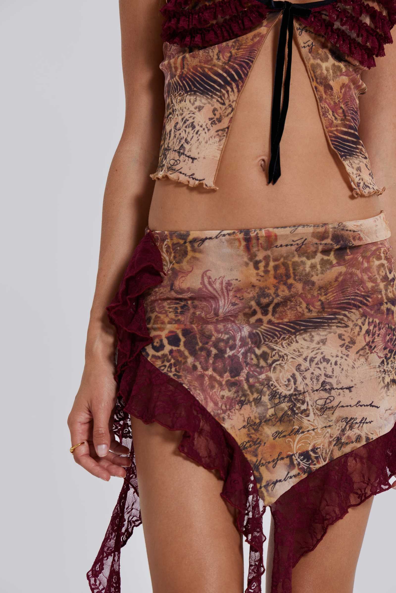 Female model wearing a leopard script print mesh mini length skirt with asymmetric hemline. Styled with the matching baby doll style top. 