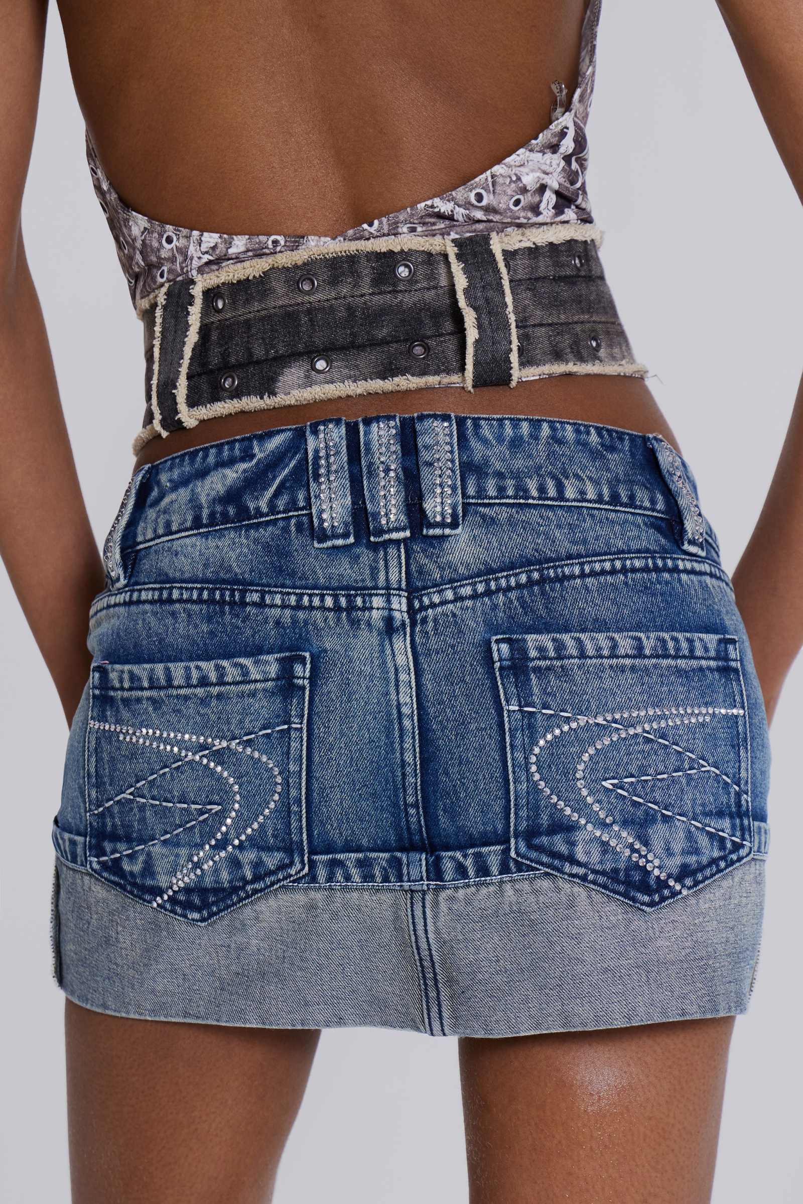 The Alexis Mini Skirt is crafted from a blue denim in a low-rise fit. The skirt features contrast stitching with an exaggerated turn-up out. The standout design is completed with functional zip pockets, diamante belt loops and exposed overlocked side seams.