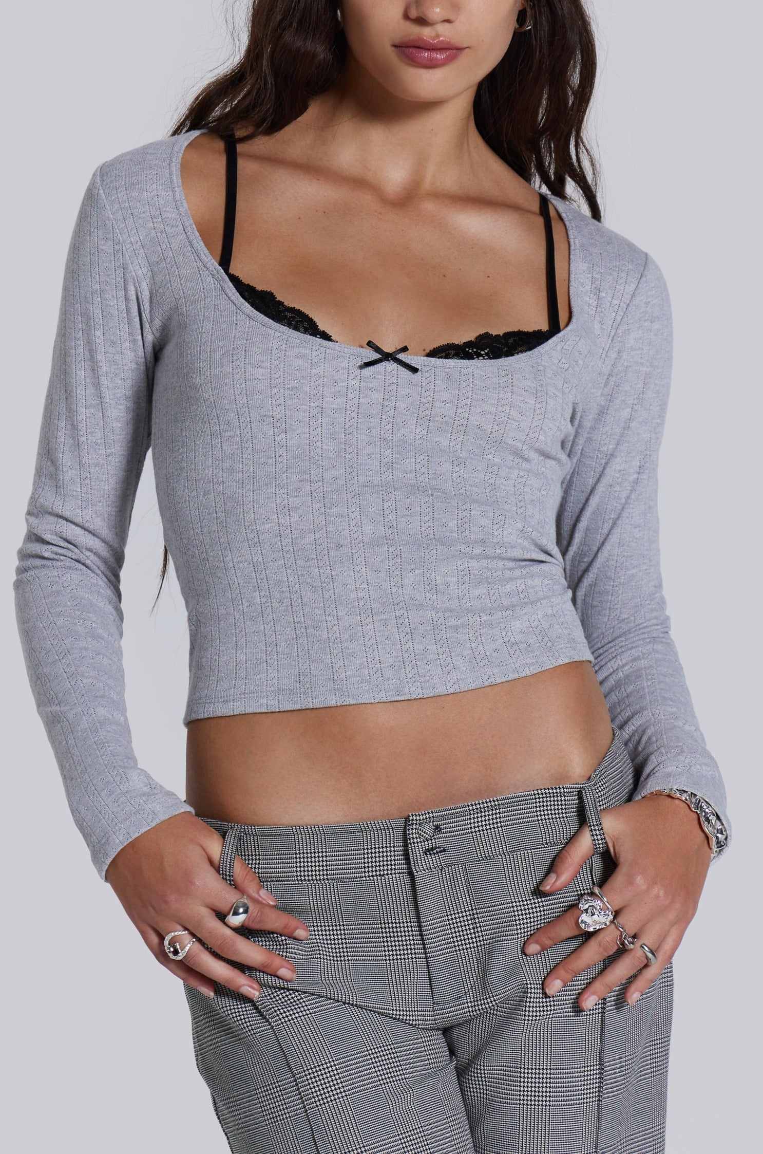 Female model wearing a grey marl long sleeve pointelle fabric with rib binding and needle neckline finish with a lace insert. 