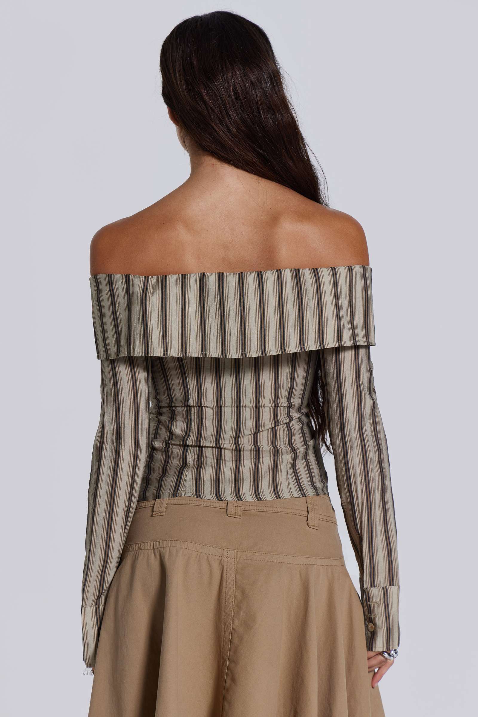  Female model wearing a khaki and brown striped off the shoulder long sleeve shirt with flared cuffs. Styled with a beige choppy cargo skirt. 